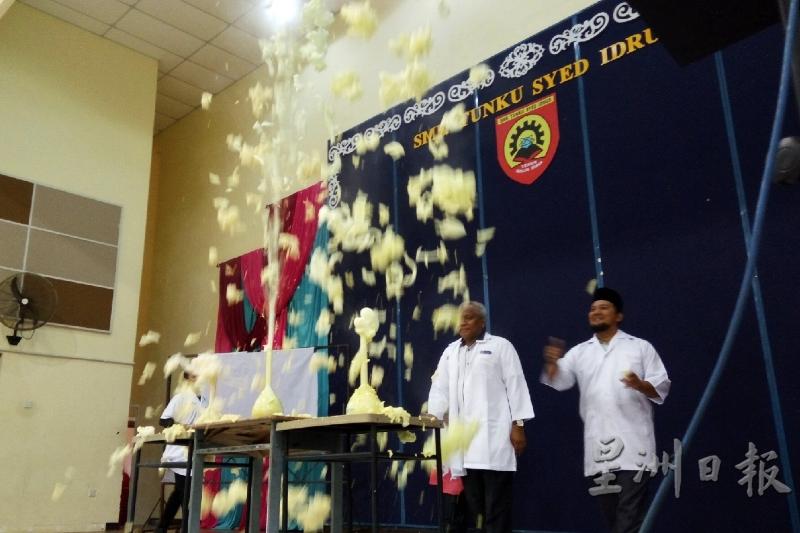 塔祖丁（左）将液体倒入容器中，使容器中的液体产生化学反应喷涌而出，场面壮观。
